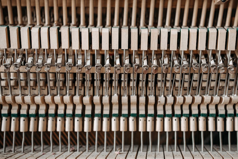 Close-up view of the interior mechanism of a piano, showing numerous hammers, strings, and felt-tipped wooden components arranged in a repeating pattern. The hammers, covered in felt, are aligned in multiple rows, ready for the pressing action. The metallic strings are visible behind the hammers, secured by tuning pins. The wooden parts and felt materials are in natural light, highlighting the detailed craftsmanship. The setting appears to be indoors within a property, timed during a home relocation or furniture transport operation by Man With a Van Hammersmith, who is performing a piano removal with careful packing and loading processes involved in difficult access situations, preparing the instrument for transport via a van parked nearby.